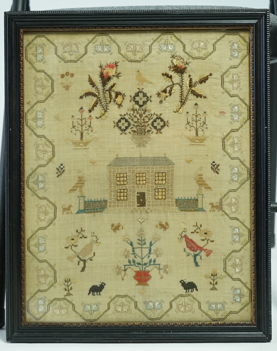 A framed 19th century needlework sampler by Ann Dunham. (undated). Worked with a large floral motif of flowering buds, above a central motif of a house with railings and two columns, with spot motifs below of dogs, peaco